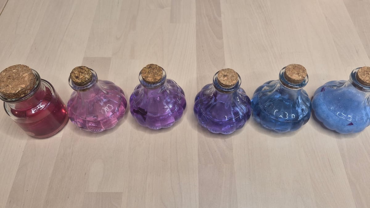Six corked potion bottles of red cabbage juice in a row, shading from deep pink through purple to blue